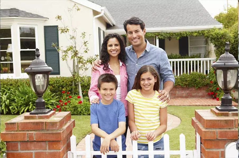 Smiling family of 4 standing in front of house