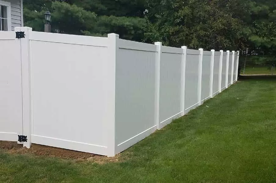 Solid white vinyl fence on green lawn with trees
